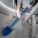 A person in gloves cleaning a stainless steel sink with a blue Carlisle Sparta brush.