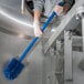 A person holding a Carlisle blue multi-purpose cleaning brush with a blue handle.