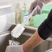 A hand in gloves using a white Carlisle bottle brush to clean a glass