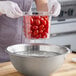 A woman using a Cambro clear plastic colander pan to drain cherry tomatoes.