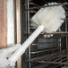 A person wearing a glove using a white Carlisle Sparta cleaning brush on a counter.