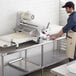 A man in a black apron and hat using an Estella countertop dough sheeter.
