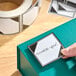 A roll of 2 1/4" x 2 1/4" blank limited quantity gloss paper permanent labels, with one label being applied to a teal box.