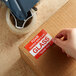 A hand using a Lavex Please Handle with Care sticker to label a box.