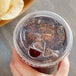 A hand holding a Choice clear plastic cup with a brown liquid and a strawless/sip lid.