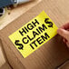 A hand using a Lavex High Claim Item label to mark a cardboard box.
