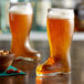 Two Stolzle beer boot glasses filled with beer on a table in a bar.