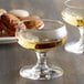 A Stolzle liqueur glass full of liquid on a table next to a plate of cookies.