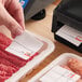A roll of white pre-printed permanent direct thermal labels being applied to packaged meat products.
