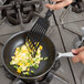 A person cooking scrambled eggs in a Vollrath Wear-Ever non-stick fry pan with a white handle.