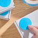 A roll of 2-inch light blue gloss paper permanent round inventory labels being applied to white boxes.