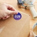 A hand using a Lavex Sunday Blue Matte Paper Inventory Day Label sticker on a cardboard box.