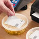 A white blank permanent direct thermal label being applied to a plastic food container.