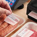 A roll of pre-printed permanent direct thermal labels for safe handling instructions, being applied to packaged meat products.