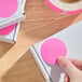 A roll of 2-inch fluorescent pink matte paper round inventory labels being applied to white boxes.