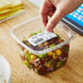 A hand holding a Globe E10 white blank label over a plastic container of food.