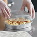 A person in gloves putting a plastic lid on a ChoiceHD aluminum foil container of food.