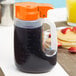 A Tablecraft plastic dispenser jar with an orange lid filled with black liquid.