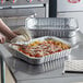 A person preparing food in a Choice foil rectangular pan.