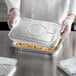 A chef putting a Choice half size aluminum foil lid on a tray of food.