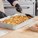 A person using a Choice deep foil steam table pan to prepare food.