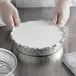 A person in gloves holding a Choice round aluminum foil pan with a board lid.