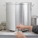 A person using a faucet to pour water into a large Vollrath aluminum stock pot.