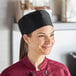 A woman wearing a black Uncommon Mesh Top Chef Skull Cap with a hook and loop closure on a professional kitchen counter.