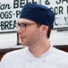 A man wearing an Uncommon Navy Blue chef skull cap with a hook and loop closure.