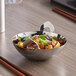 A Vollrath mini stainless steel wok with food on a table.