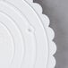 A white plastic Wilton cake separator plate with scalloped edges.