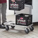 A man using a Regency milk crate dolly to move black plastic crates.