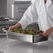 A chef holding a Carlisle stainless steel perforated steam table pan filled with green and purple lettuce over a counter.