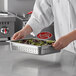 A chef holding a Carlisle stainless steel pan filled with vegetables.