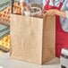 A woman in a red apron holding a Duro Grande natural kraft paper shopping bag full of food.