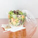 A salad in a Dart clear plastic container with a white fork on a napkin.