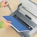 A hand using a Fellowes Quasar manual wire binding machine to bind a blue book.