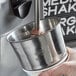 A hand using a Mercer Culinary stainless steel malt cup collar to hold a metal malt cup.