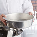 A person holding a Vollrath stainless steel water pan filled with water.