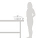 A woman standing next to a white table with a Vollrath round stainless steel water pan on it.