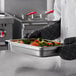 A chef holding a Carlisle stainless steel pan with vegetables.