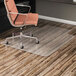 An Alera clear office chair mat under a chair at a desk with wood floors.