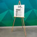 A wooden Aarco easel with a white sign on it.