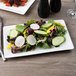 A white rectangular porcelain plate with a salad of radishes and carrots on a table.