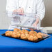 A chef opening a clear Cal-Mil rectangular tray cover to reveal pastries.