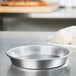 An American Metalcraft aluminum deep dish pizza pan with dough on a counter.