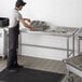 A man in a black apron standing at a Regency stainless steel sorting table.