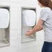 A woman using a Lavex Stainless Steel ADA Compliant recess kit for a hand dryer.