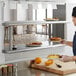 A woman in a chef's uniform using a Regency stainless steel pass-through shelf to hold plates of food.