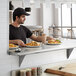A man sitting at a counter with a plate of food on a Regency stainless steel pass-through shelf.